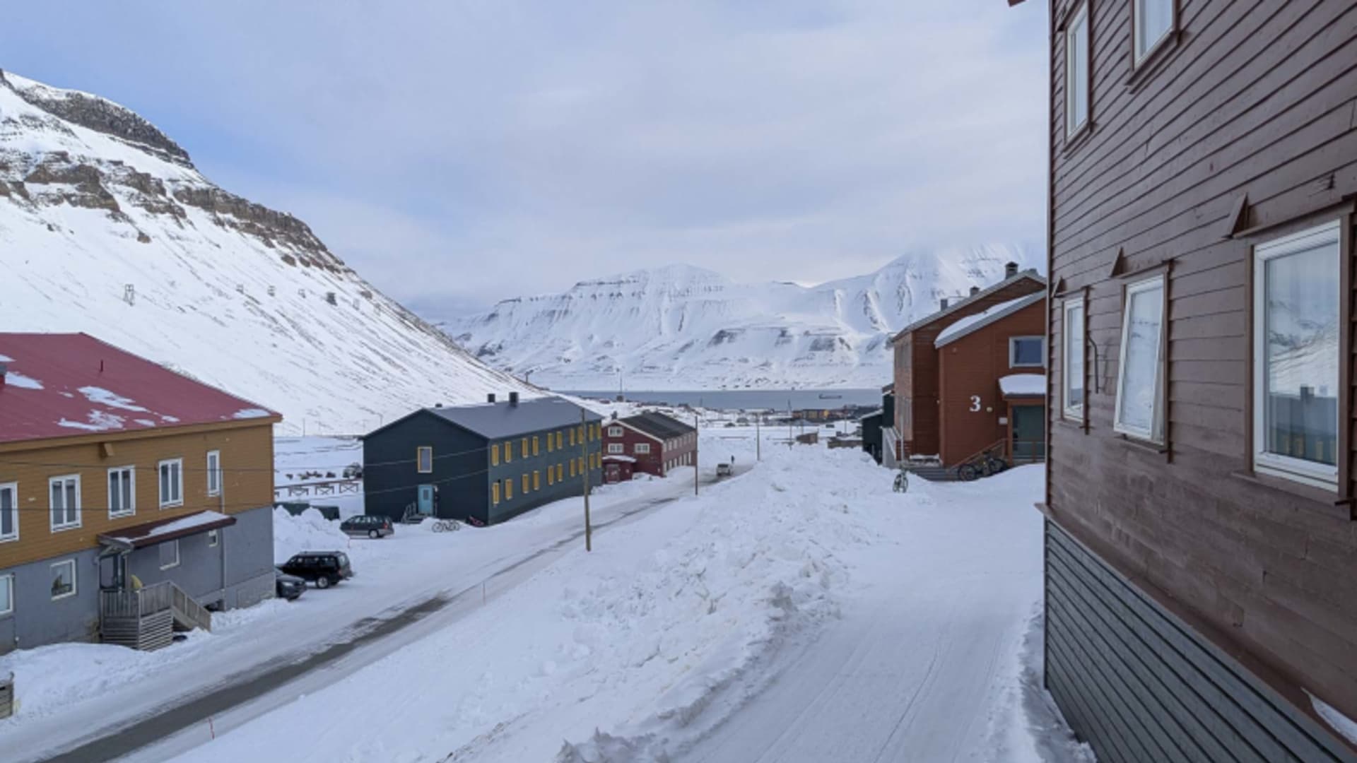 Straßenansicht des Coal Miners Hotel - Longyearbyen zwischen bunten Holzhäusern in verschneiter Siedlung.