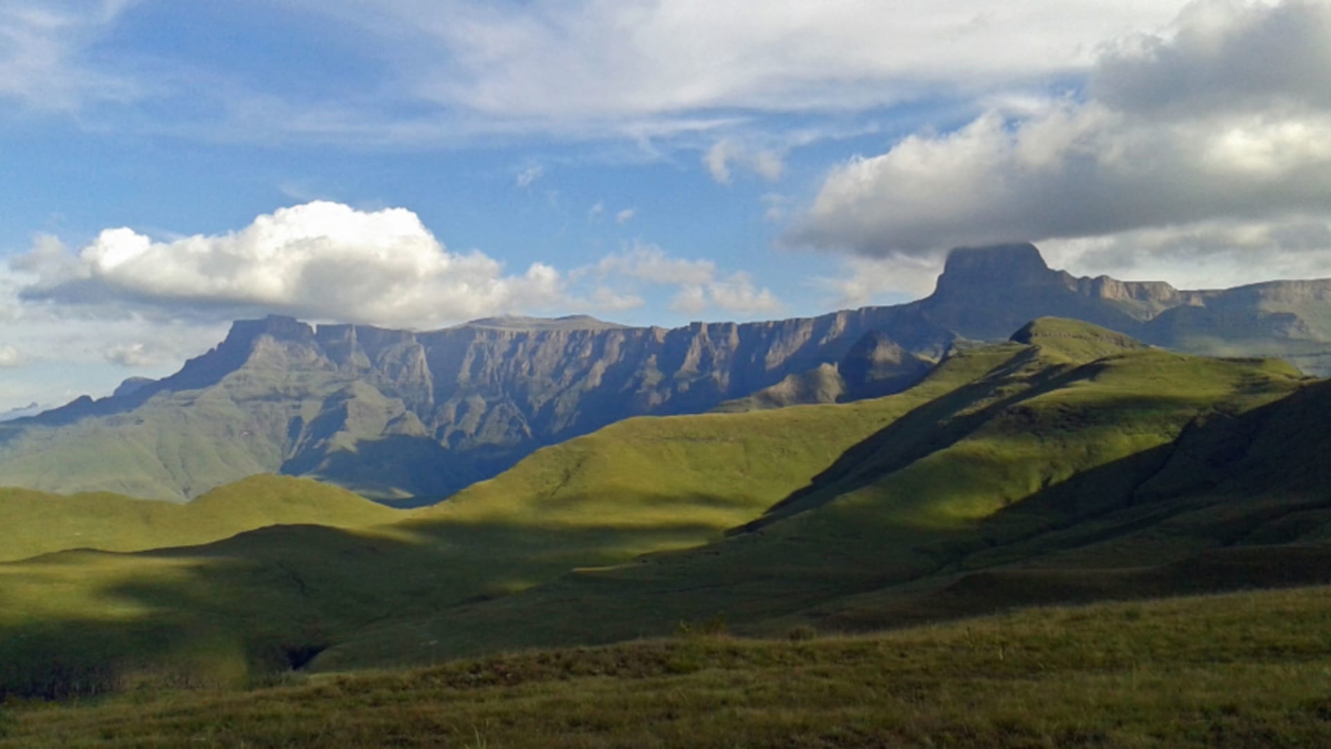 Blick über grüne Hochland-Graslandschaft auf das Tafelberg-Massiv mit isoliertem Felsturm im Maloti-Drakensberg Park nahe der Witsieshoek Mountain Lodge.