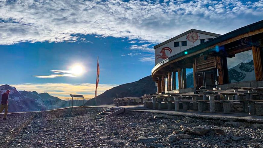 Das Berghaus Diavolezza steht auf einem Felsgrat mit Terrasse und Schweizer Flagge bei Sonnenschein.