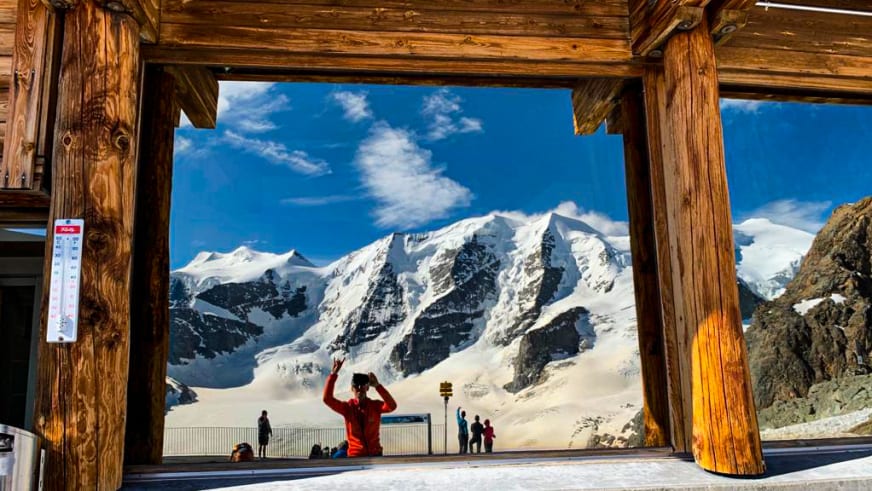 Blick aus dem Berghaus Diavolezza durch die Holzkonstruktion auf Besucher und vergletscherte Berggipfel.