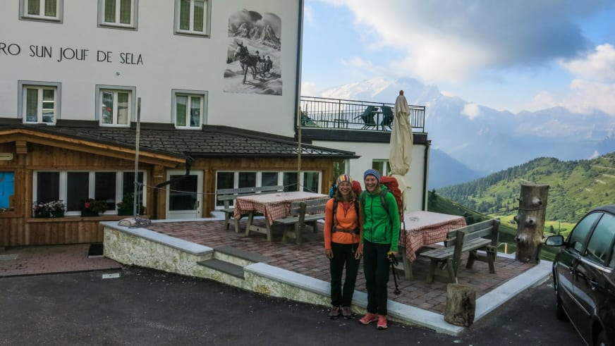 Zwei Bergwanderer mit Rucksäcken vor dem Rifugio Carlo Valentini am Sellajoch.