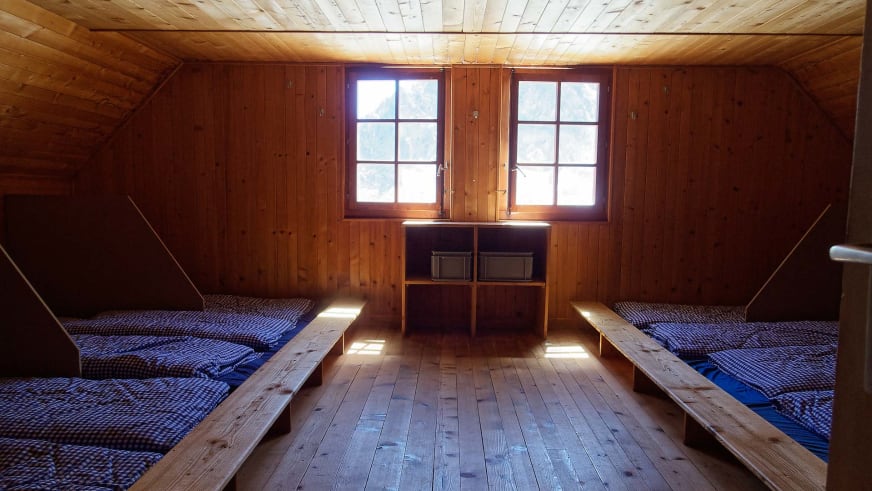 Holz-Matratzenlager unter der Dachschräge der Cabane du Trient mit karierten Matratzen und Doppelfenster.