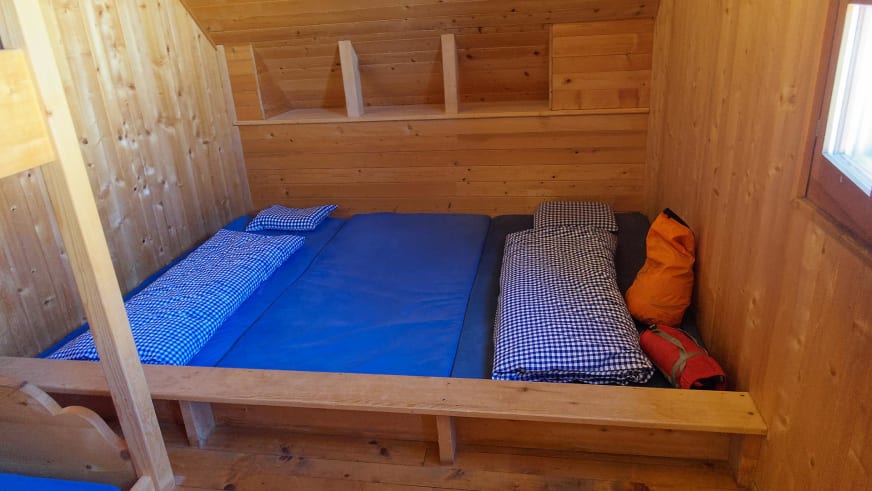Etagenbett aus Holz in der Cabane du Trient mit blauer Bettwäsche und orangefarbenen Schlafsäcken.