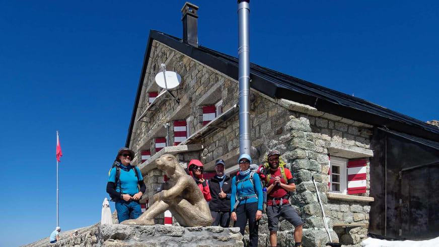 Fünf Bergwanderer posieren vor dem Natursteinbau der Cabane du Trient mit rot-weißen Fensterläden.