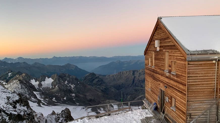 Außenansicht der Marco e Rosa Hütte in Holzbauweise mit beleuchteten Fenstern und weitem Blick über verschneite Gipfel d