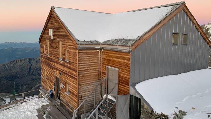 Die Marco e Rosa Hütte zeigt moderne Bergarchitektur mit Holz- und Metallverkleidung bei Abenddämmerung in schneebedeckt
