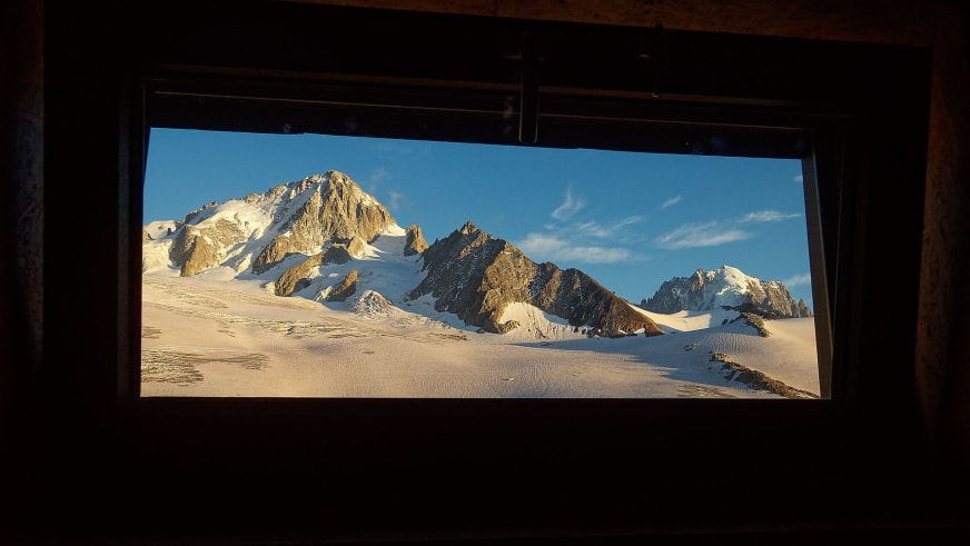 Blick durch das Panoramafenster des Refuge Albert 1er auf die verschneite Gletscherlandschaft des Hochgebirges.