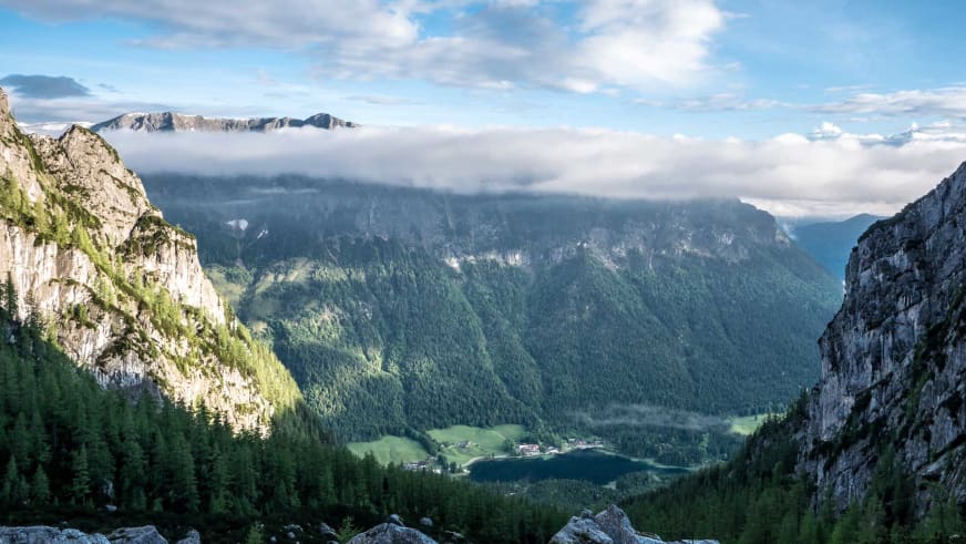 Panoramablick von der Blaueishütte ins bewaldete Tal mit Siedlung und Bergkette im Hintergrund.