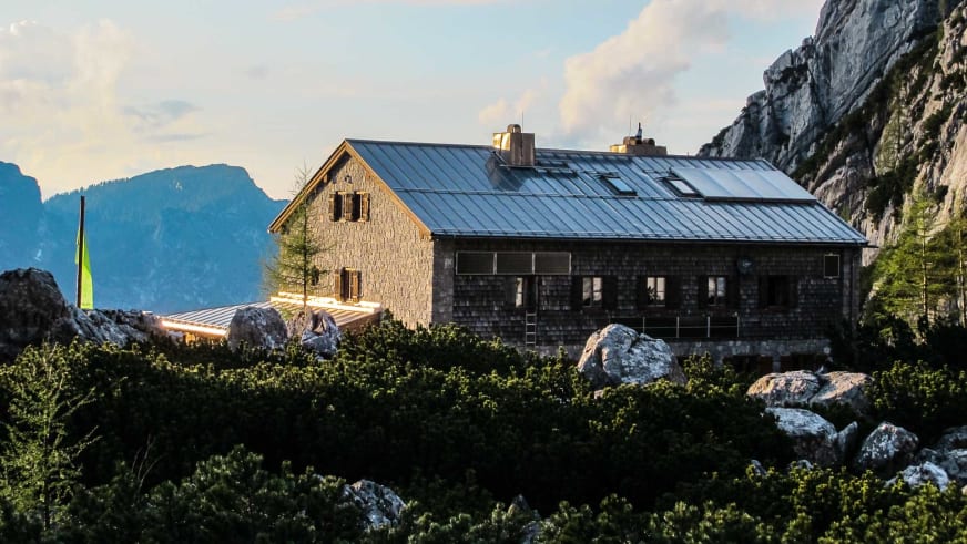 Die Blaueishütte bei Abendlicht mit Stein- und Holzbau vor steilen Felswänden.