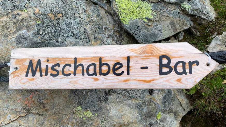 Handgefertigtes Holzschild mit der Aufschrift 'Mischabel - Bar' auf einer Steinmauer an der Mischabelhütte.
