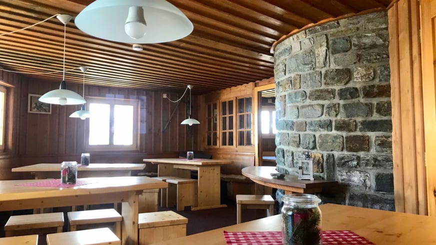 Gastraum der Domhütte mit Holztischen, Steinofen und karierter Tischdekoration im alpinen Stil.