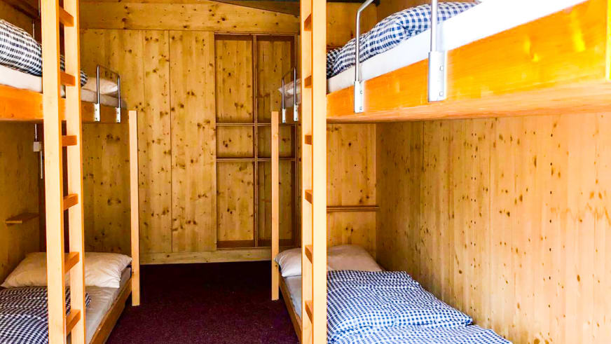 Mehrbettzimmer der Domhütte mit drei Etagenbetten aus Fichtenholz, Kleiderschrank und vollständiger Holzverkleidung an Wänden und Decke.