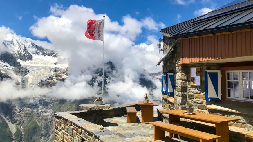 Terrasse der Domhütte auf 2940 m mit Holzbänken vor vergletscherten Gipfeln der Walliser Alpen.