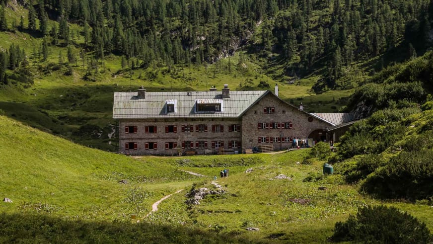 Zwei Bergwanderer mit Rucksäcken gehen auf dem Wanderweg zum Kärlingerhaus durch die grüne Almwiese.