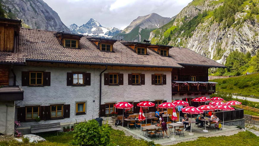Gäste entspannen auf der Sonnenterrasse des Lucknerhaus mit roten Sonnenschirmen und Bergpanorama.