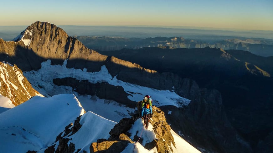 Zwei Bergsteiger klettern am schneebedeckten Felsgrat bei der Finsteraarhornhütte in den Berner Alpen bei Sonnenaufgang.