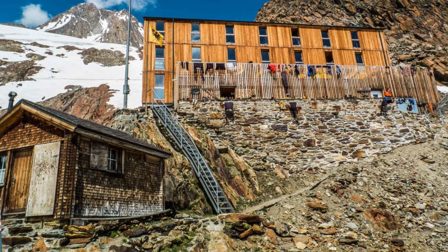 Zweiteiliges Gebäude der Finsteraarhornhütte mit Holzfassade und Balkon in steiler Felswand-Umgebung.