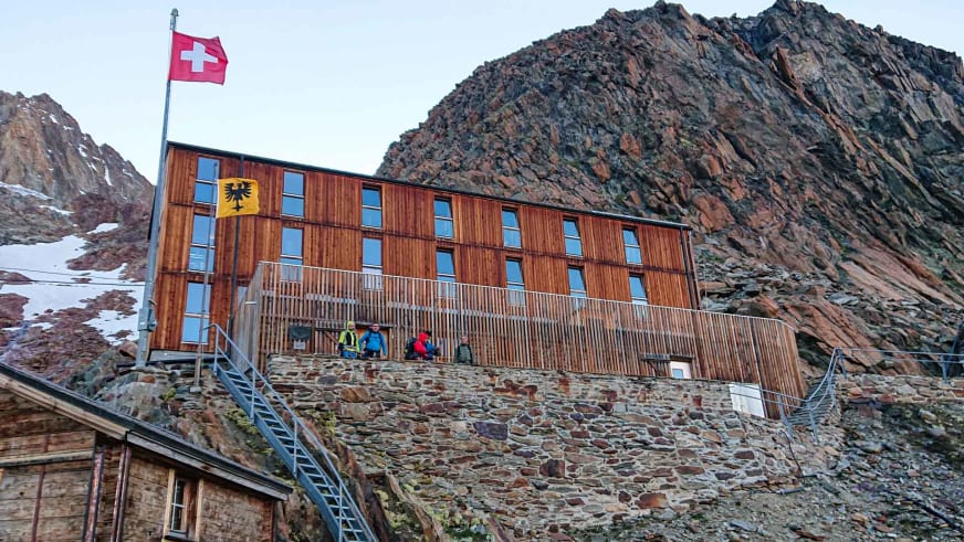 Fünf Bergsteiger in bunter Kleidung stehen vor der Finsteraarhornhütte mit ihrer charakteristischen Holz-Stein-Fassade.