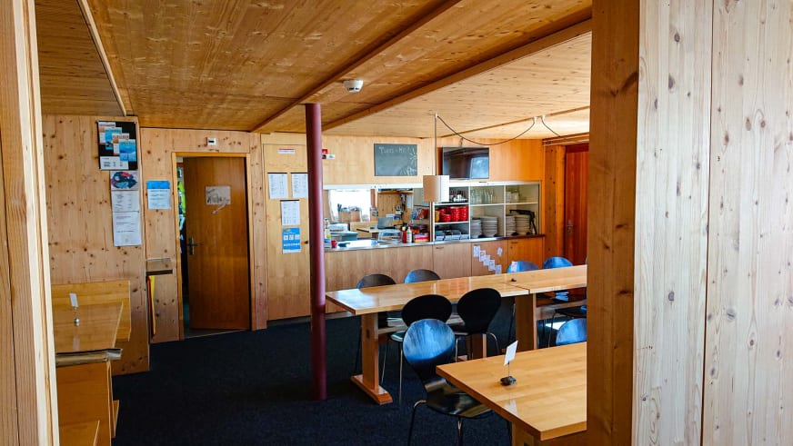Bergsteiger finden warme Atmosphäre im Gastraum der Finsteraarhornhütte mit Holztischen und traditioneller Einrichtung.