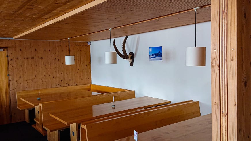 Heller Gastraum der Finsteraarhornhütte mit Fichtenholz-Tischen und weißen Pendelleuchten unter Holzdecke.