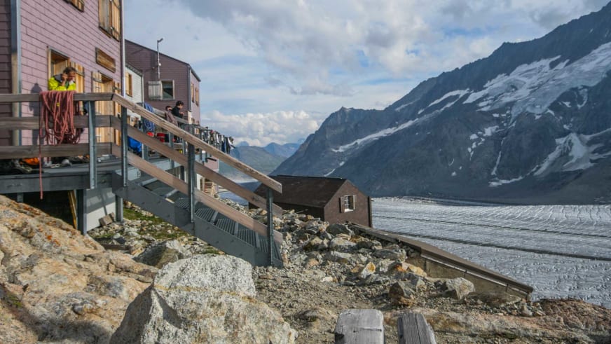 Bergsteiger vor der Konkordiahütte mit rosa-grauer Fassade direkt am Gletscherrand.