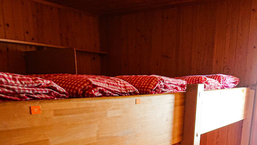 Schlafraum der Konkordiahütte mit Etagenbetten aus hellem Holz und rot-weiß karierter Bettwäsche.