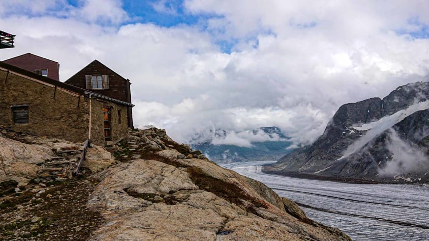 Panoramablick auf die Konkordiahütte auf einem Felsplateau mit dem Aletschgletscher im Hintergrund.