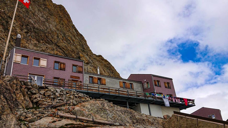 Die Konkordiahütte mit rotbrauner Holzverkleidung und Schweizer Flagge am steilen Felsabhang.