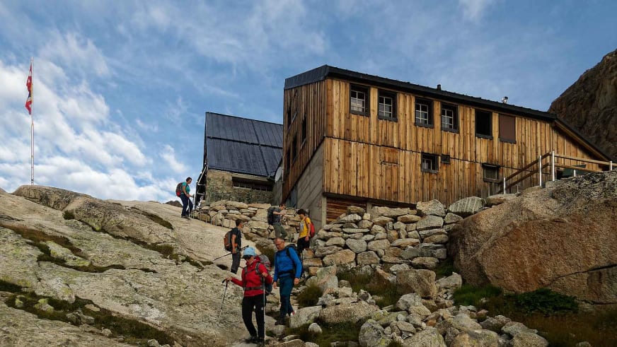Wandergruppe mit Rucksäcken und Wanderstöcken bewegt sich zwischen Granitblöcken vor der Cabane d'Orny.