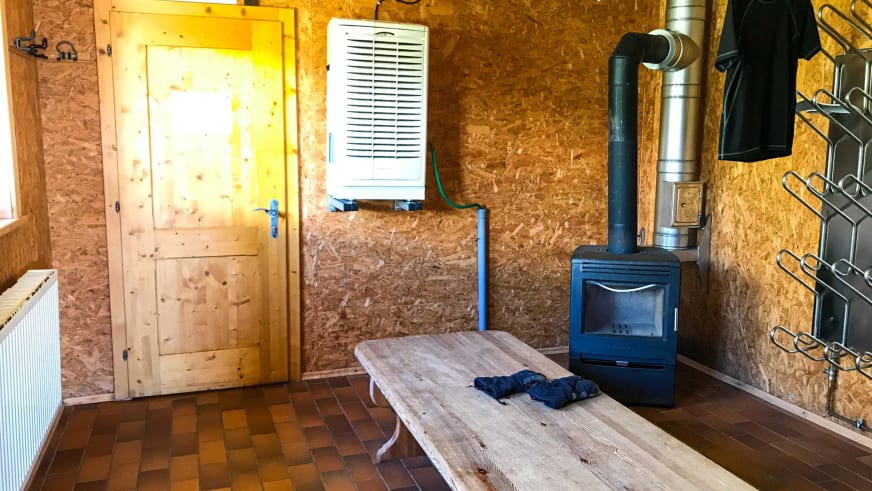 Trockenraum der Vernagthütte mit schwarzem Kaminofen und Holztisch zum Trocknen der Ausrüstung.