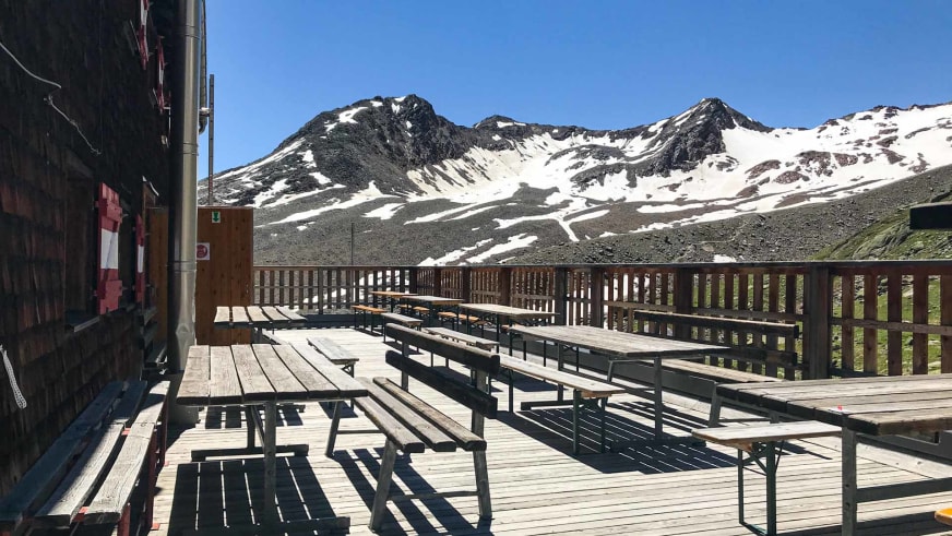 Sonnenterrasse der Vernagthütte mit Holzbänken und Panoramablick auf die verschneiten Ötztaler Alpen.