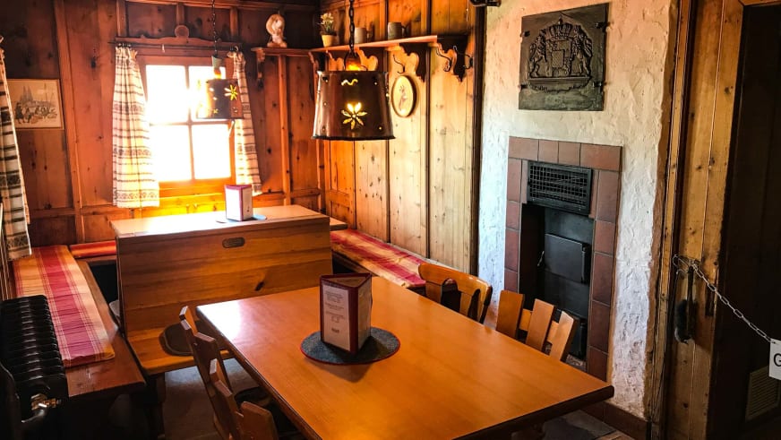 Gaststube der Vernagthütte mit zentralem Esstisch und traditionellem Kachelofen aus braunen Kacheln.