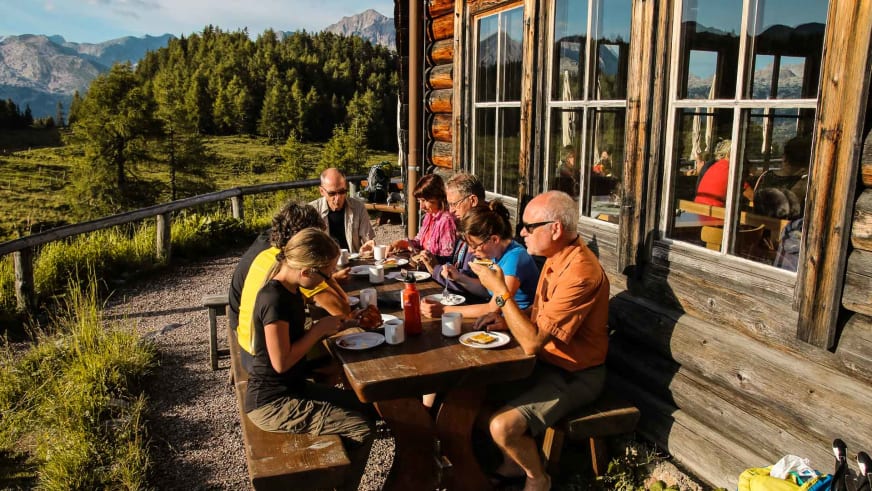 Wanderer beim Frühstück auf der Holzterrasse der Gotzenalm mit Blick auf die Berchtesgadener Alpen.