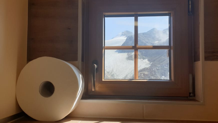 Toilette der Similaunhütte mit Holzfenster und direktem Blick auf die verschneiten Gletscher der Umgebung.