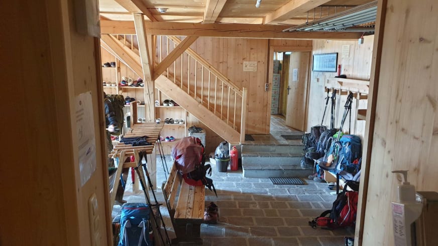 Eingangsbereich der Similaunhütte mit Holztreppe, Schuhregalen und abgestellter Bergausrüstung.
