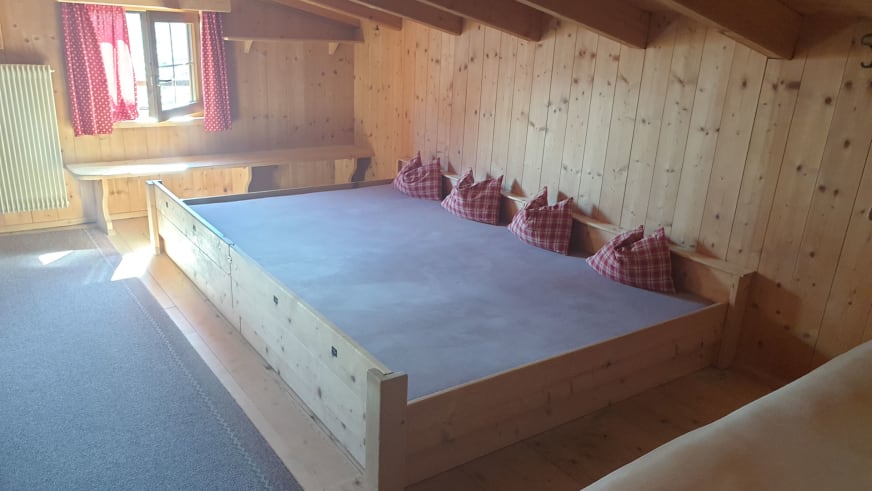 Schlafraum der Similaunhütte mit Holzbett, rot-weiß karierten Kissen und traditioneller Holzverkleidung.