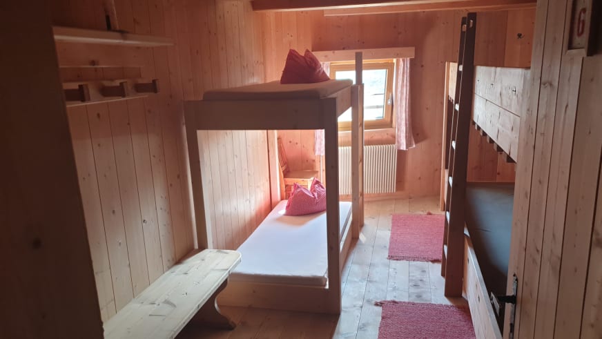 Mehrbettzimmer der Similaunhütte mit Etagenbett aus Massivholz, Holzbank und rot karierten Textilien.
