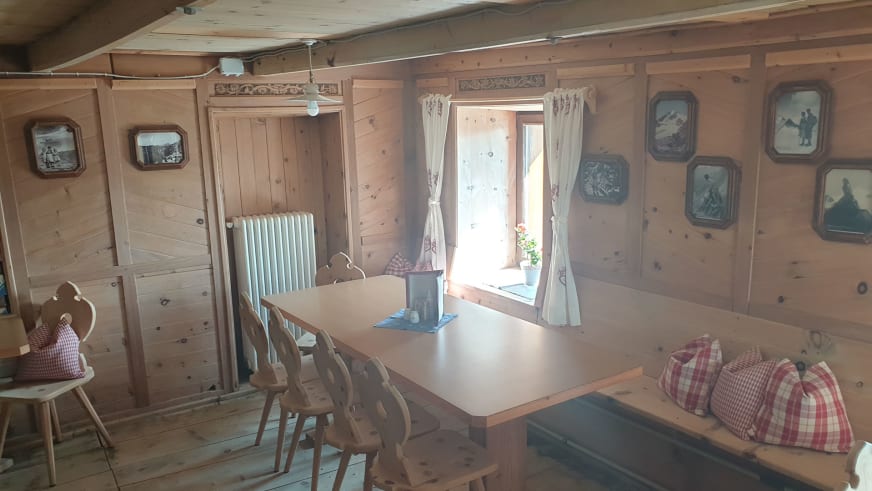 Speiseraum der Similaunhütte mit traditioneller Eckbank, Holztisch und gerahmten Bergbildern an den Wänden.