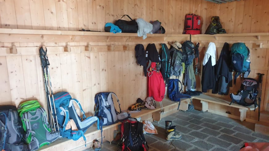 Trockenraum der Similaunhütte mit Garderobenhaken, Rucksäcken und Bergausrüstung an Holzwänden.