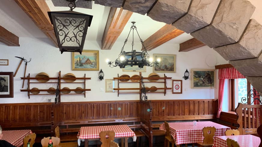 Gemütliche Gaststube im Tičarjev dom na Vršiču mit Holzvertäfelung und rot-weiß karierten Tischdecken.