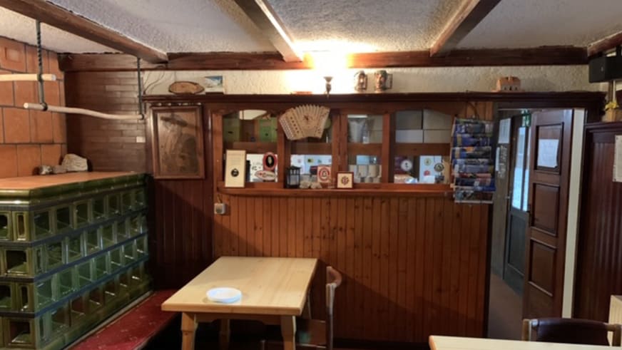 Innenbereich vom Tičarjev dom na Vršiču mit Holztheke und gekacheltem Ofen in der Gaststube.