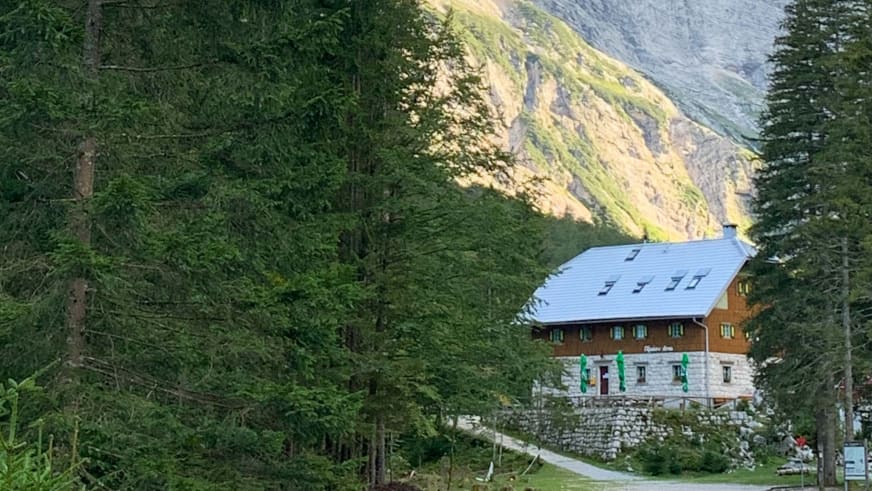 Bergsteiger vor dem Aljažev dom v Vratih mit traditioneller Bauweise aus Naturstein und Holz zwischen Fichten.