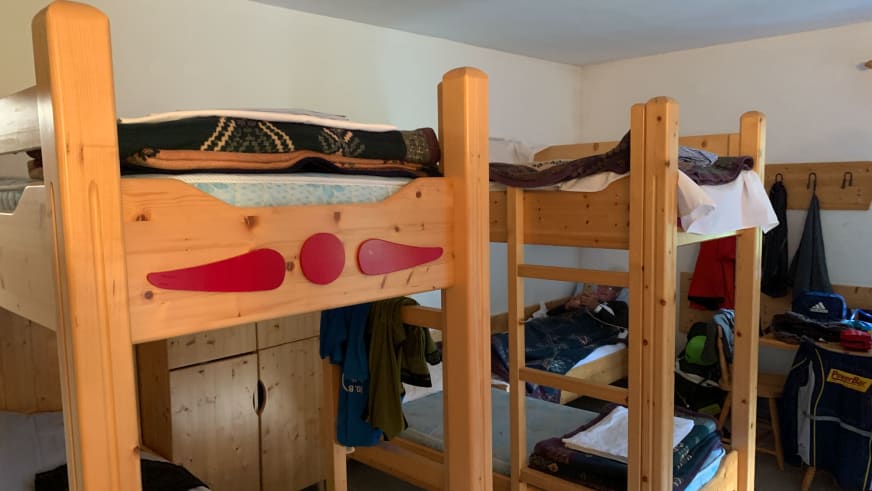 Schlafsaal im Aljažev dom v Vratih zeigt mehrere Stockbetten aus hellem Holz mit bunter Bettwäsche und persönlichen Gege