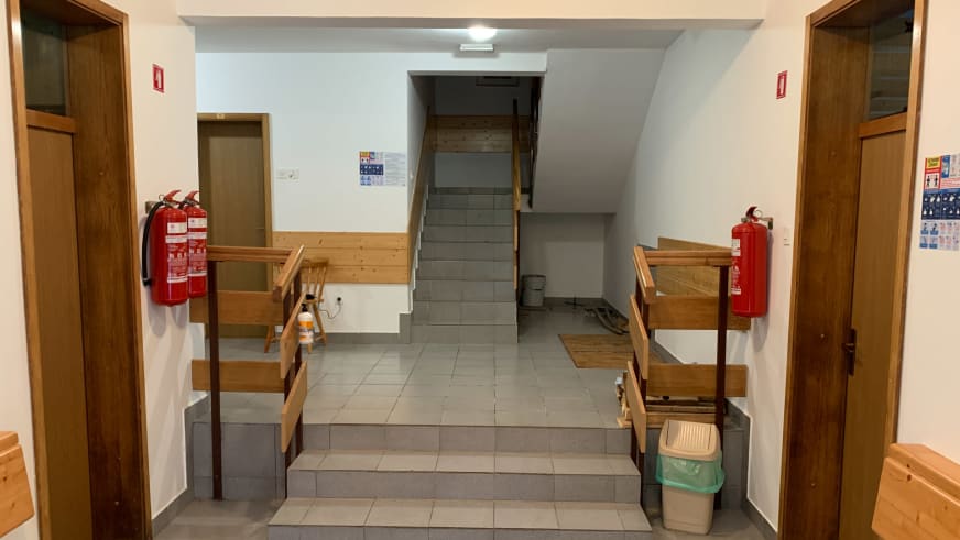 Eingangshalle im Aljažev dom v Vratih mit zentraler Steintreppe und Holzbänken zum Schuhwechsel an den Seiten.