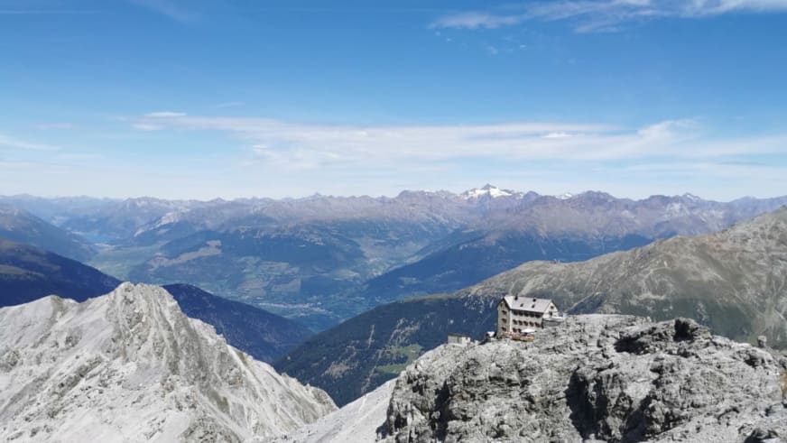 Sommerpanorama zeigt das Rifugio Casati auf zerklüftetem Felssockel mit Blick über mehrere schneebedeckte Bergketten.