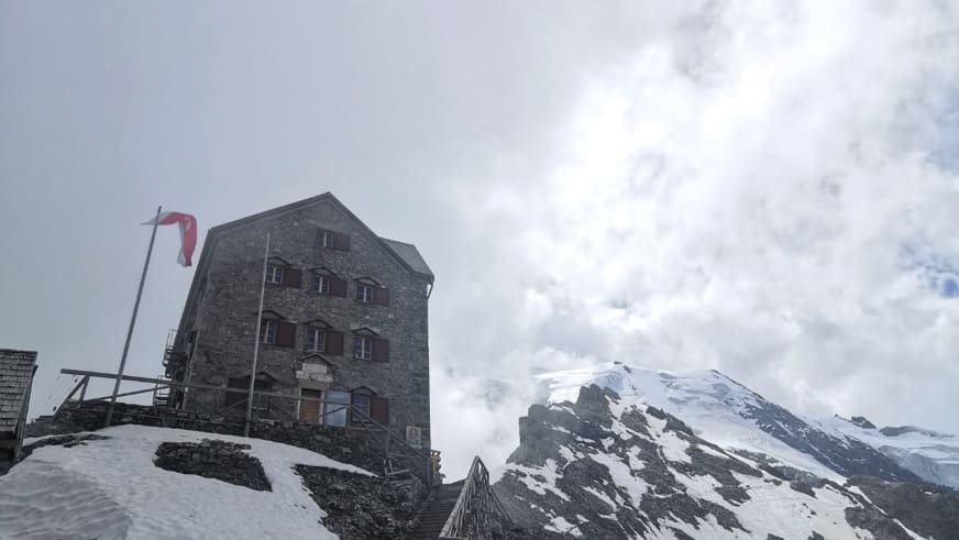 Das Rifugio Casati zeigt traditionelle Steinarchitektur mit grauem Satteldach vor schneebedecktem Berggipfel bei bewölkt
