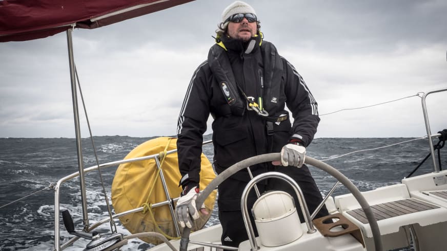 Bergführer Hans Honold in schwarzer Segeljacke und gelber Rettungsweste steuert ein Segelboot bei bewölktem Wetter auf dem Meer.