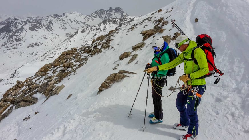 Bergführer Markus Beck und eine Person stehen mit Tourenski auf steilem Firnhang, beide tragen Helme und Klettergurte.