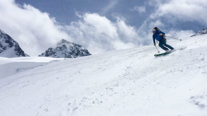 Bergführer Markus Beck fährt in blauer Skijacke einen steilen schneebedeckten Hang hinab vor Hochgebirgskulisse.