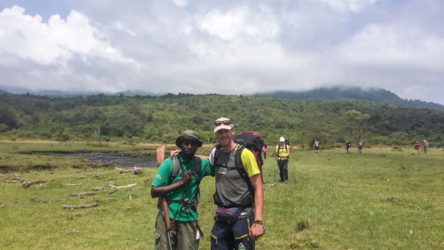Zwei Männer mit Trekking-Rucksäcken stehen auf grüner Hochebene, einer davon Bergführer Markus Beck in grauem Shirt.